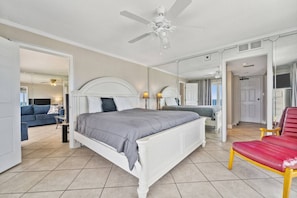 A bedroom with a large bed, a red chair, a ceiling fan, and a mirror reflecting the room.