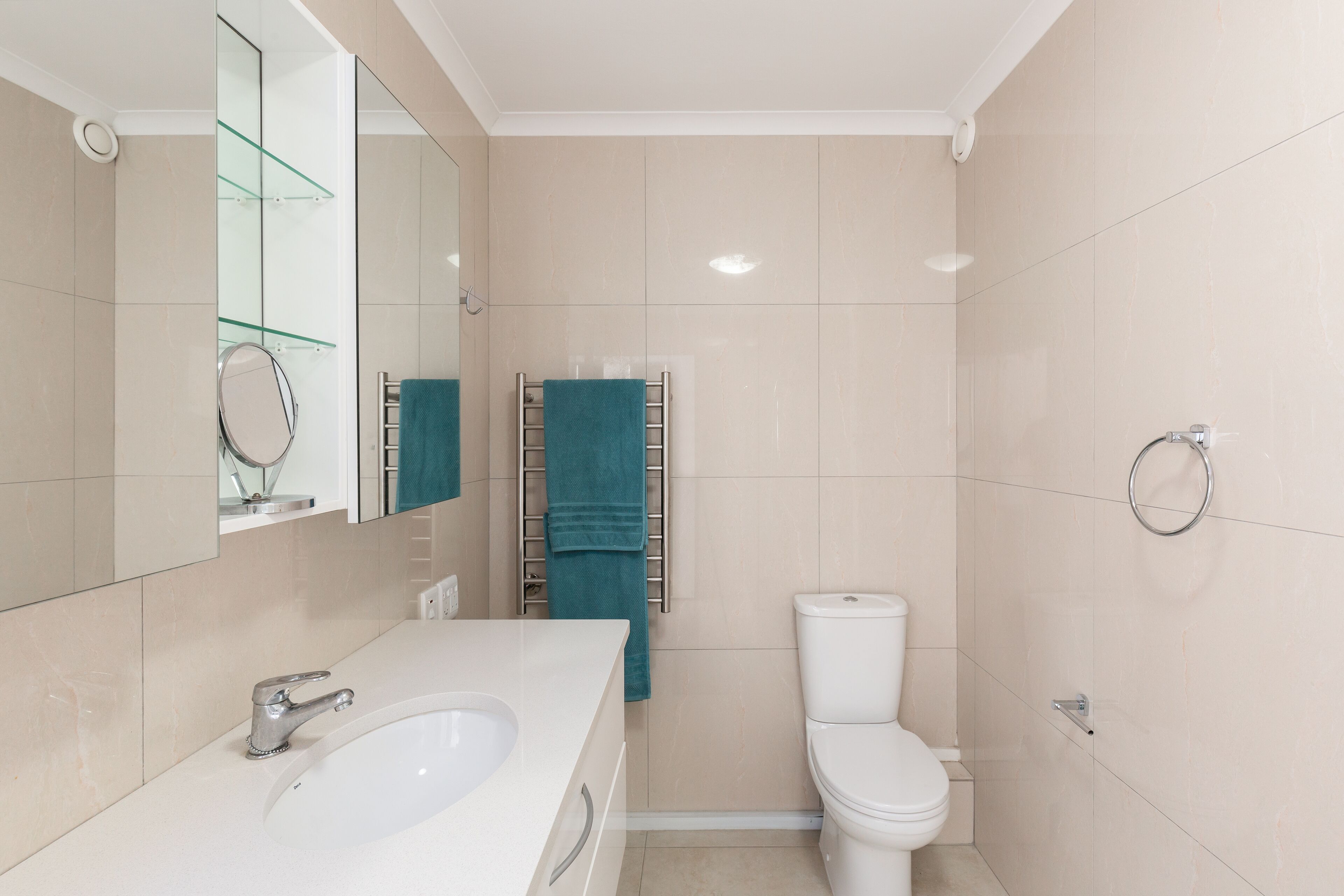 A modern bathroom with a white sink, a toilet, and a glass shelf.
