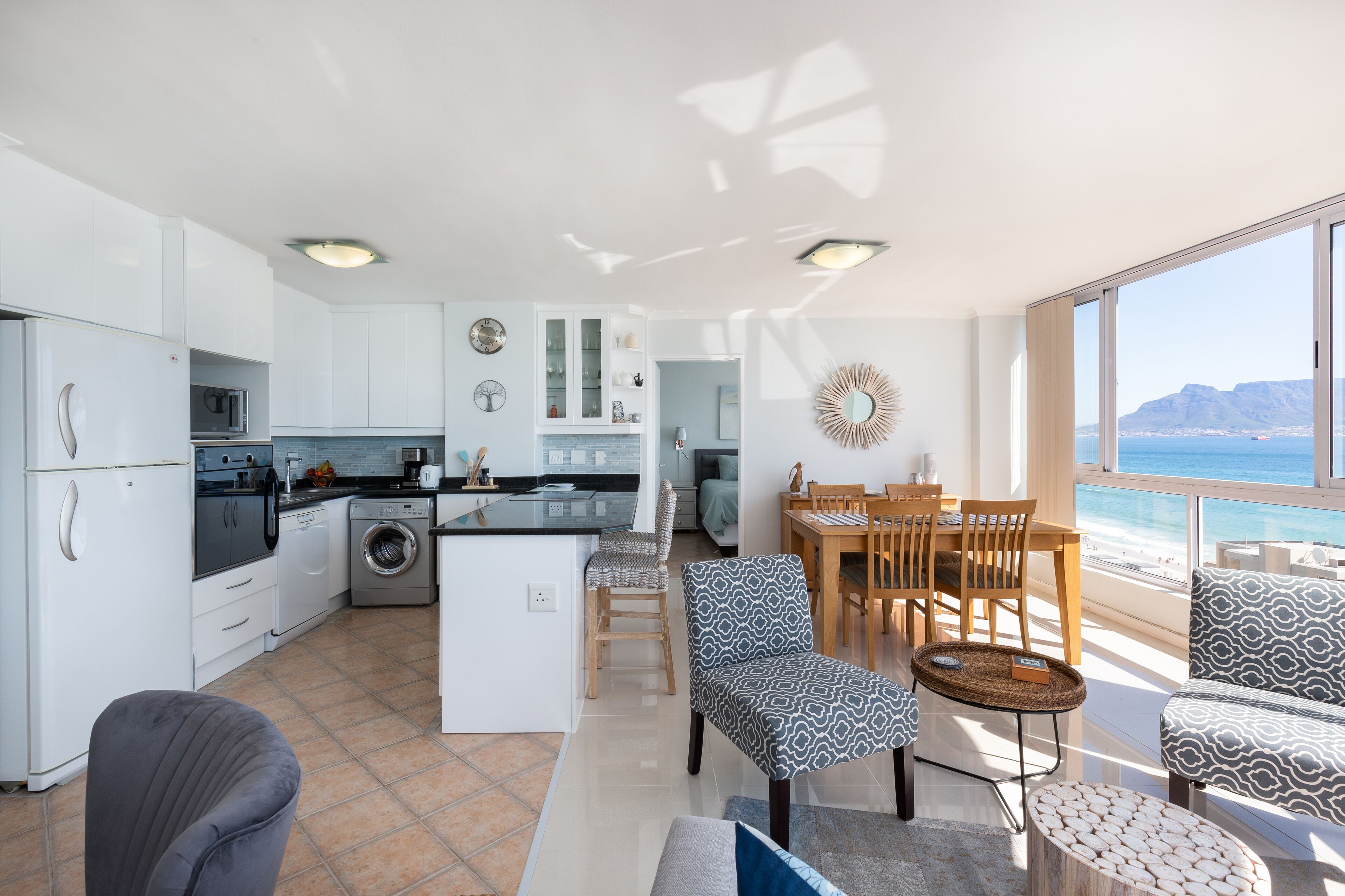 A modern kitchen with a central island, dining area with wooden furniture, and a view of the ocean.