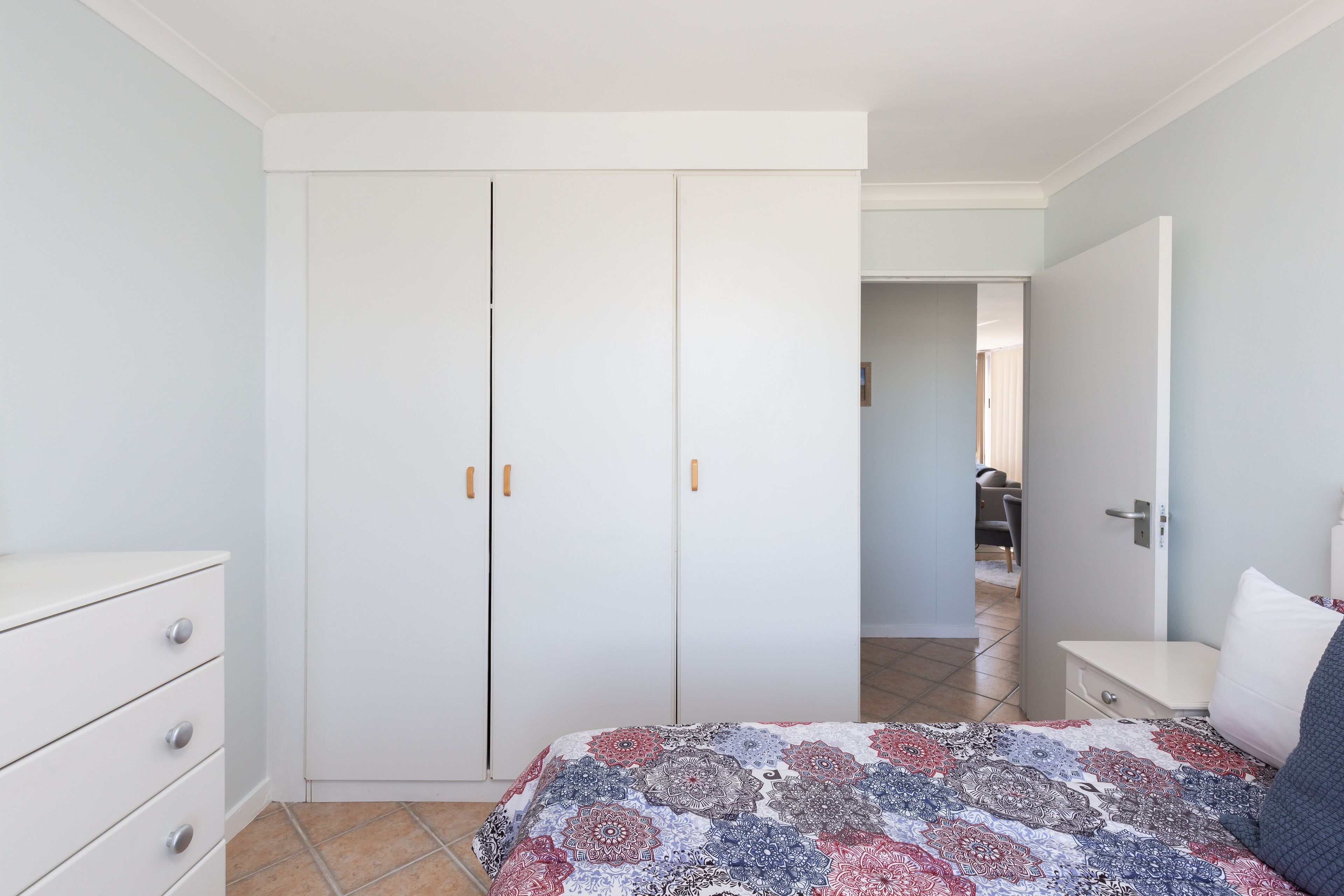 A bedroom with a bed, a dresser, a wardrobe, and a bedside table.