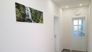 Een gang met een witte deur, een aan de muur hangend horloge en een lijst met een foto van een waterval.