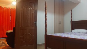 A bedroom with a wooden four-poster bed, a closed door with intricate carvings, and a red curtain partially visible. - South B 1 bedroom rental furnished apartment  (Nairobi)