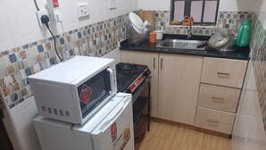 A compact kitchen with a refrigerator, microwave, stove, sink, and tiled backsplash. - South B 1 bedroom rental furnished apartment  (Nairobi)