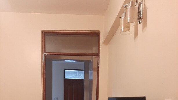 A living room with a sofa, a flat-screen TV mounted on the wall, and a hallway leading to a door. - South B 1 bedroom rental furnished apartment  (Nairobi)