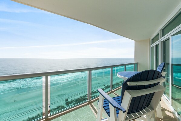 Enjoy the ocean view from this balcony with two chairs and a table.