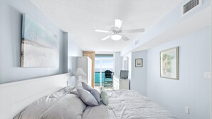 Ein Schlafzimmer mit einem Bett, einem Deckenventilator und Meerblick durch eine Schiebetür.