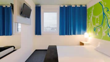A hotel room with a bed, a desk, a chair, a TV, and a window with curtains.