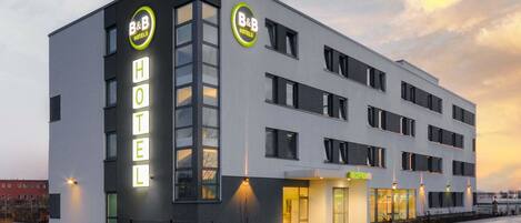 A modern B&B hotel with a prominent 'HOTEL' sign, multiple windows, and a well-lit entrance.