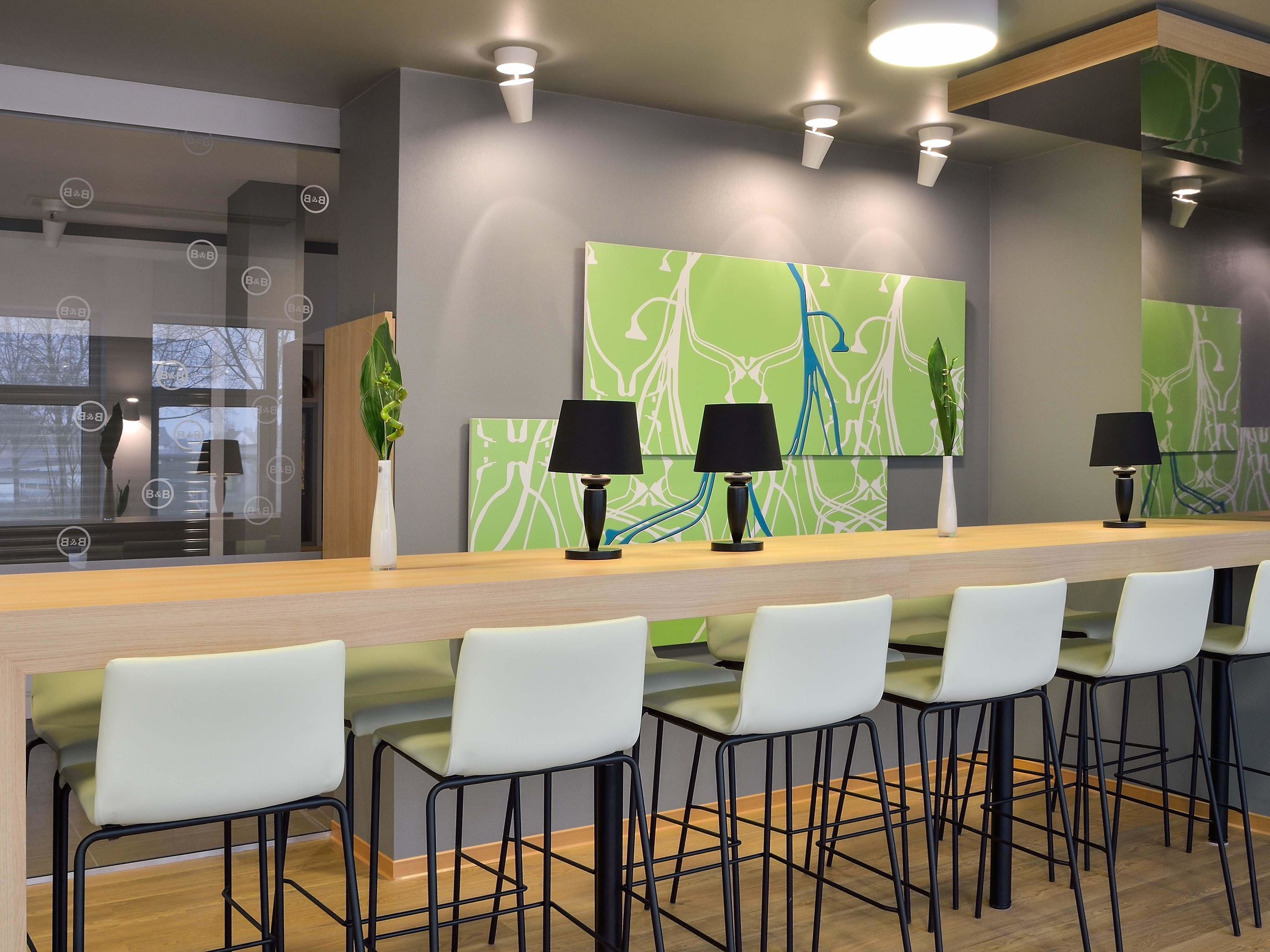 A modern bar area with a long counter, black chairs, and green abstract wall art.