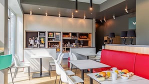 A modern cafe with white tables and chairs, a red booth, and a variety of food and drink options. - B&B Hotel Hamburg-Nord (Hamburg)