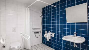 A bathroom with a white toilet, a shower with a white curtain, a blue tiled wall, and a white sink.