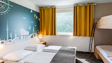 A hotel room with a bed, a desk, a lamp, a window with curtains, and a wall mural.