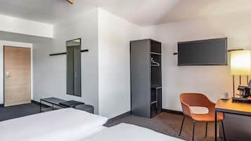 A hotel room with a bed, a desk, a chair, a wardrobe, a mirror, and a TV.