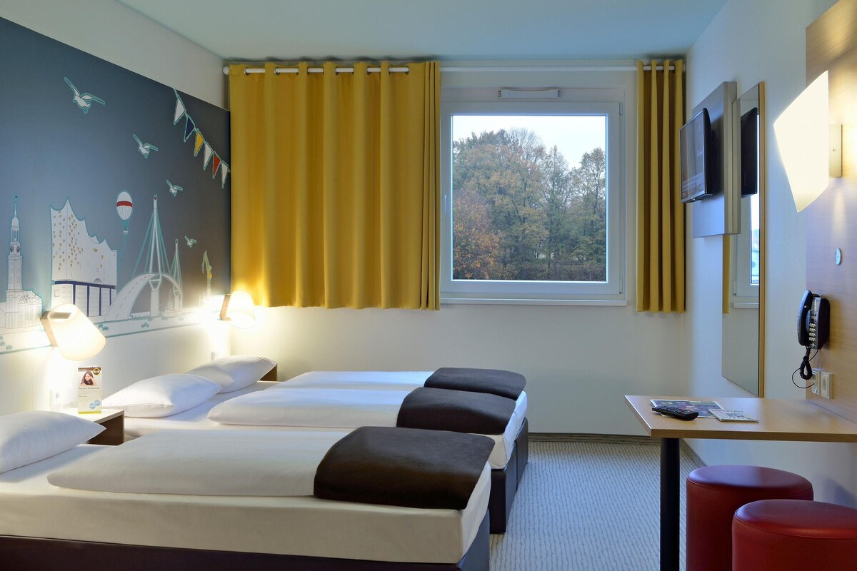 A hotel room with two beds, a desk, a telephone, and a window with a view of trees.