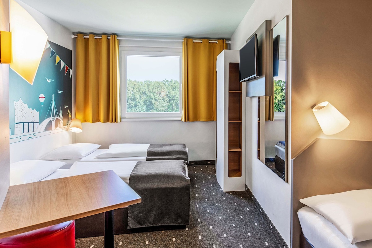 Une chambre d’hôtel avec un lit, un bureau, une télévision et une fenêtre avec des rideaux.