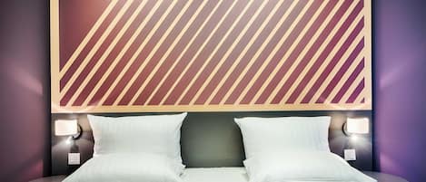 A hotel room with a large bed, two bedside tables with lamps, and a patterned wall above the bed.