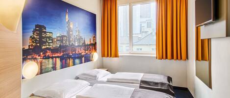 A hotel room with two beds, a large window with orange curtains, a cityscape mural on the wall, and a flat-screen TV mounted on the wall.