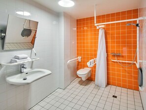 A bathroom with white and orange tiles, a sink, a toilet, a shower with a curtain, and a mirror. - B&B Hotel Frankfurt-Hbf (Frankfurt)