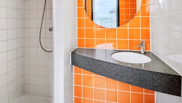 A bathroom with white tiled walls, an orange-tiled accent wall, a round mirror, and a sink with a black countertop.