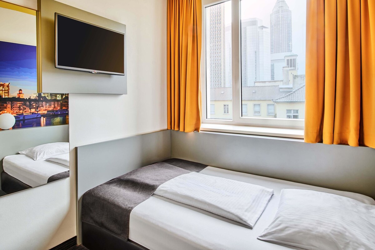 A hotel room with a bed, a TV mounted on the wall, and a window with curtains.