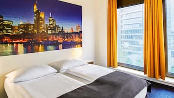 A hotel room with a bed, a cityscape painting, a window with curtains, and a view of buildings.