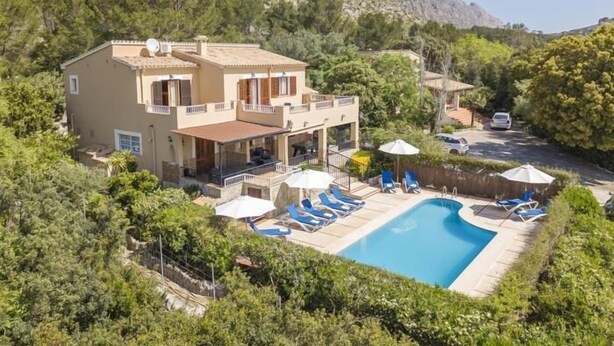 Una casa de dos pisos con piscina, rodeada de follaje y con montañas al fondo.
