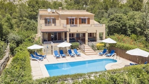 Una casa de dos pisos con piscina, rodeada de vegetación y montañas.