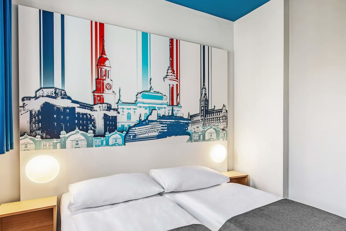 A hotel room with a bed, a nightstand, and a large cityscape artwork on the wall.