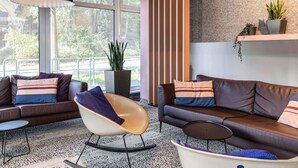 A modern living room with leather sofas, a unique chair, and a large window offering a view of greenery. - B&B Hotel Hamburg City-Ost (Hamburg)