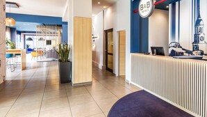 A modern hotel reception area with a blue and white color scheme, a reception desk, and a seating area with chairs and a potted plant. - B&B Hotel Hamburg City-Ost (Hamburg)
