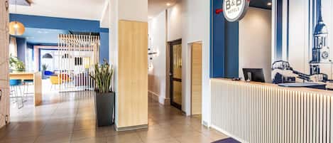 Uma área de recepção de hotel moderna, com esquema de cores azul e branco, balcão de recepção e uma área de estar com cadeiras e uma planta em vaso.