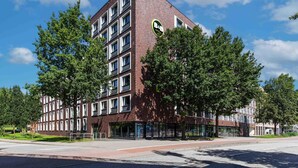 A modern hotel with a brick facade, multiple windows, and a green circular logo. - B&B Hotel Hamburg City-Ost (Hamburg)