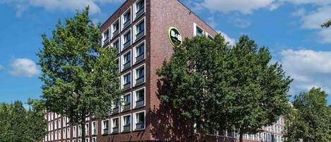 Un hôtel moderne avec une façade en briques, de nombreuses fenêtres et un logo circulaire vert.