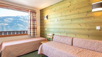 A room with two beds, a wooden wall, a window with a view of mountains, and a balcony railing.