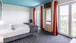 Una habitación de hotel moderna con una cama, un televisor en la pared y ventanas grandes con cortinas.