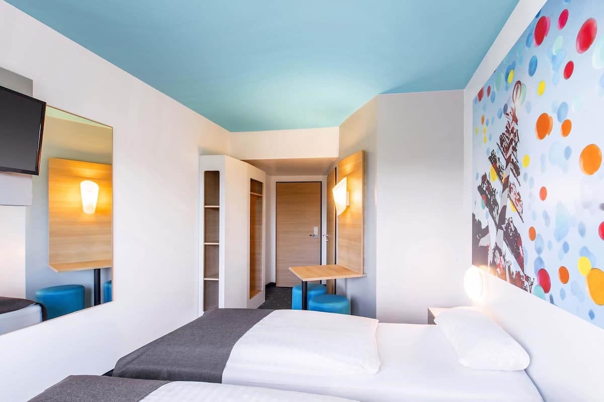 A hotel room with two beds, a desk, and a colorful wall mural.
