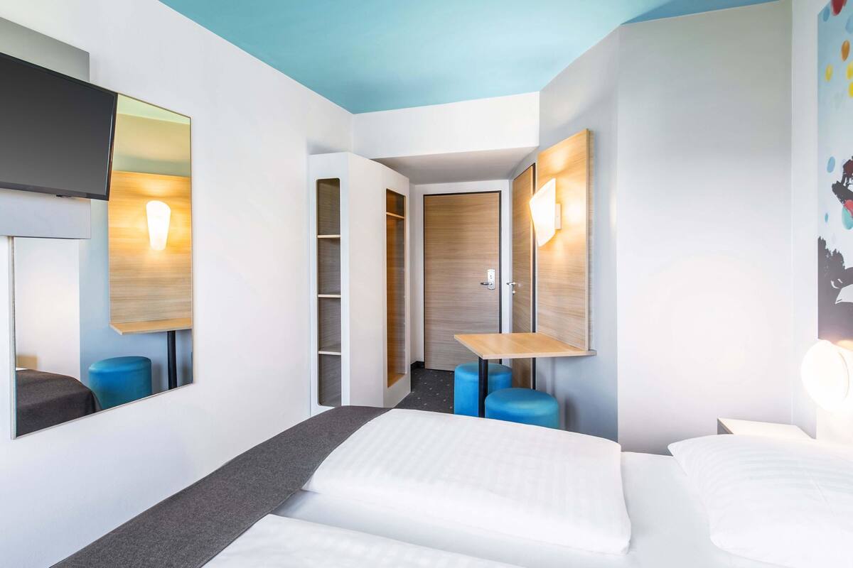 A modern hotel room with a bed, a desk, and a wardrobe.