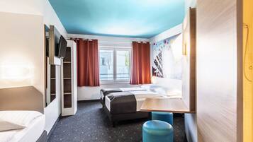 A modern hotel room with a bed, a desk, a wardrobe, and a window with curtains.