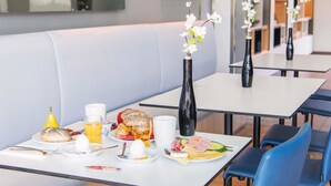Un comedor moderno con mesas blancas, sillas azules y un banco. Hay jarrones con flores sobre las mesas.