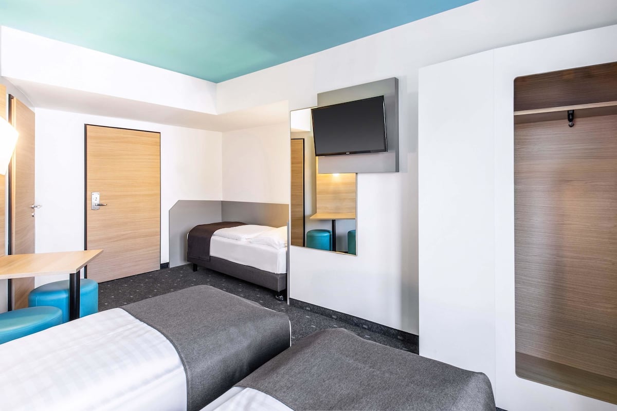 A hotel room with a bed, a desk, a TV mounted on the wall, and a wardrobe.