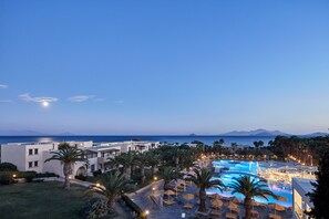 A resort with a swimming pool, palm trees, and a view of the sea.