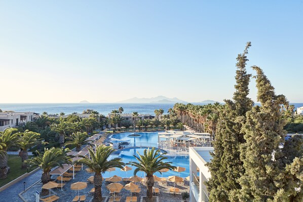 A resort pool area with palm trees, lounge chairs, and a view of the ocean.