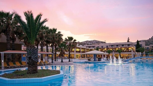 A hotel pool area with palm trees, lounge chairs, and a fountain. - Porto Bello Beach - All Inclusive (Kos)