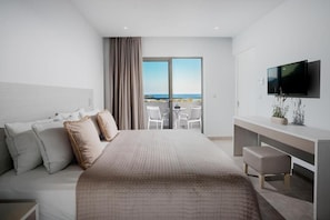 Una habitación de hotel moderna con una cama grande, un escritorio, televisión y un balcón con vistas al mar.