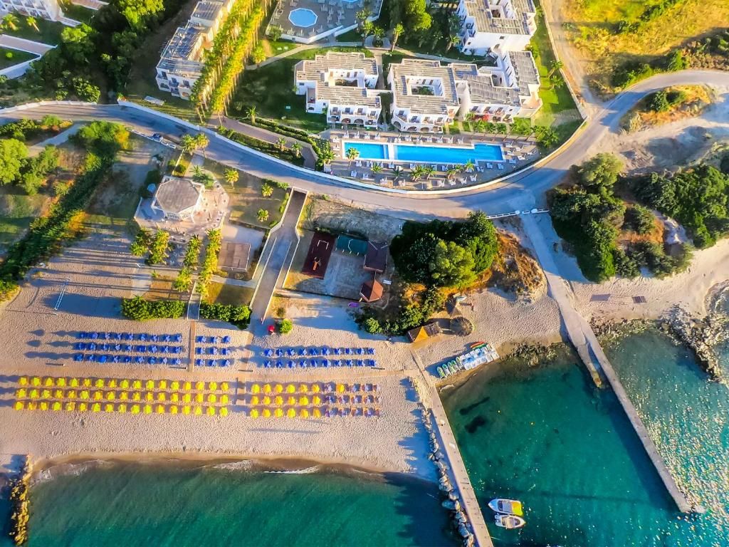 Vista aerea di un hotel sulla costa con piscina, ombrelloni da spiaggia e un molo.
