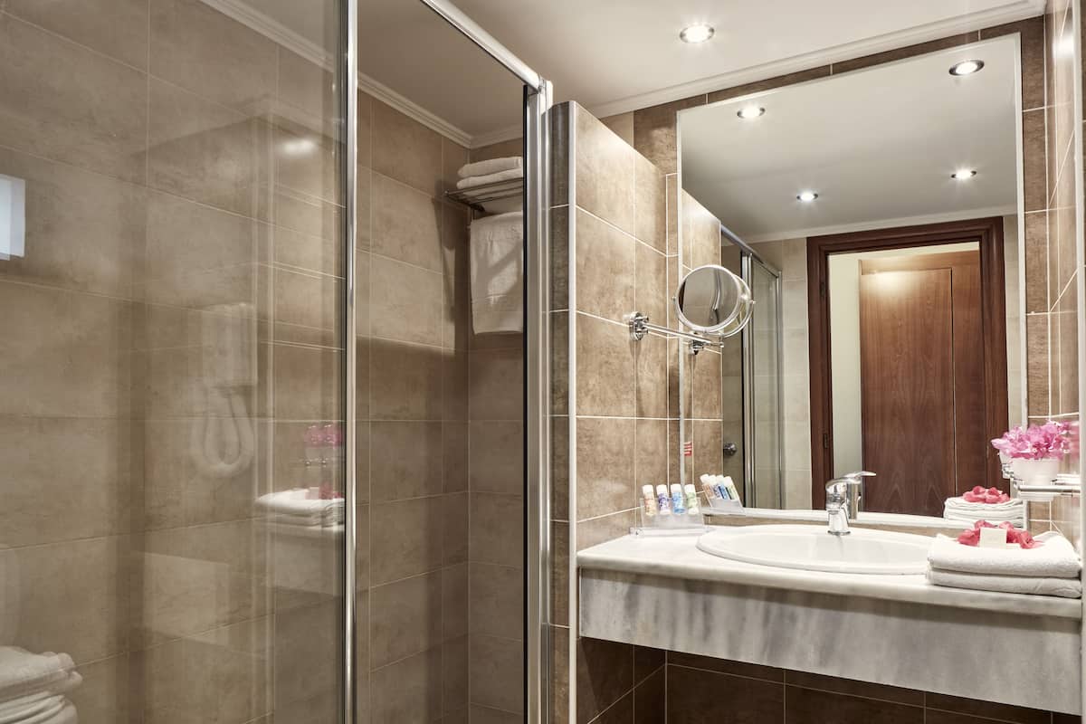 A modern bathroom with a glass shower enclosure, a large mirror, and a vanity with a sink and toiletries.