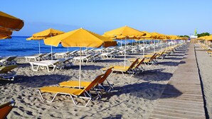 A beach with rows of sun loungers and yellow umbrellas, a wooden boardwalk, and the ocean in the background. - Porto Bello Beach - All Inclusive (Kos)