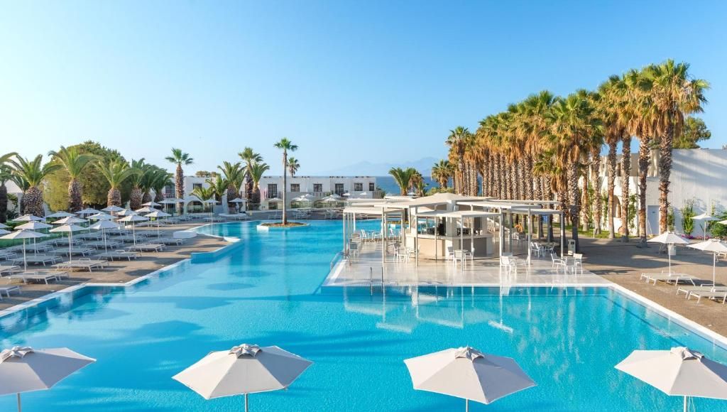 Una piscina con lettini e ombrelloni, circondata da palme e un cielo sereno.