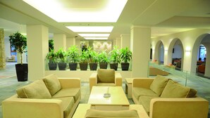 A spacious lobby with a modern design, featuring a seating area with sofas and armchairs, a coffee table, and multiple potted plants. - Porto Bello Beach - All Inclusive (Kos)