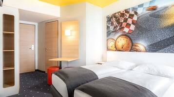 A hotel room with a bed, a desk, a chair, a wardrobe, and a wall with a racing car mural.